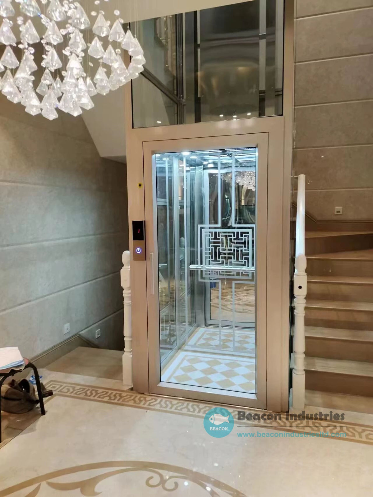 Enclosed glass home lift with a beige frame and decorative door panel beside an indoor staircase