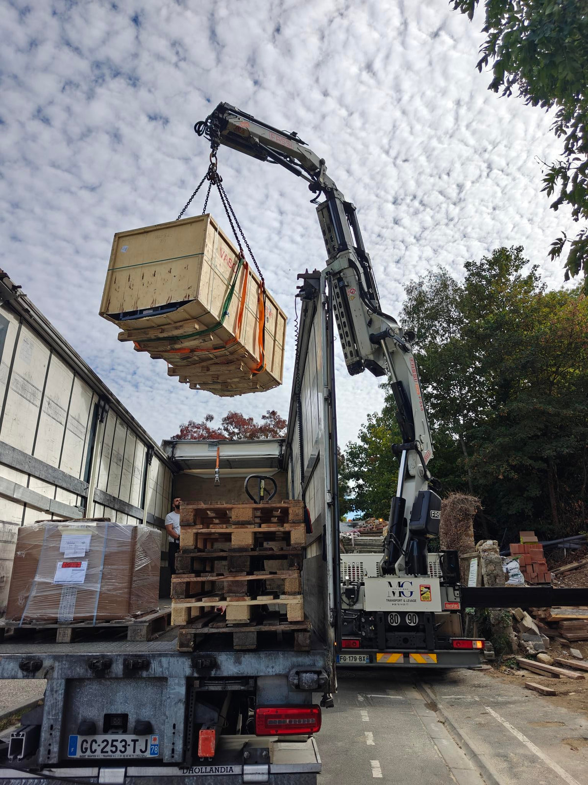 Crane unloading a wooden home lift shipping crate beside a truck, with timber base supports visible underneath.