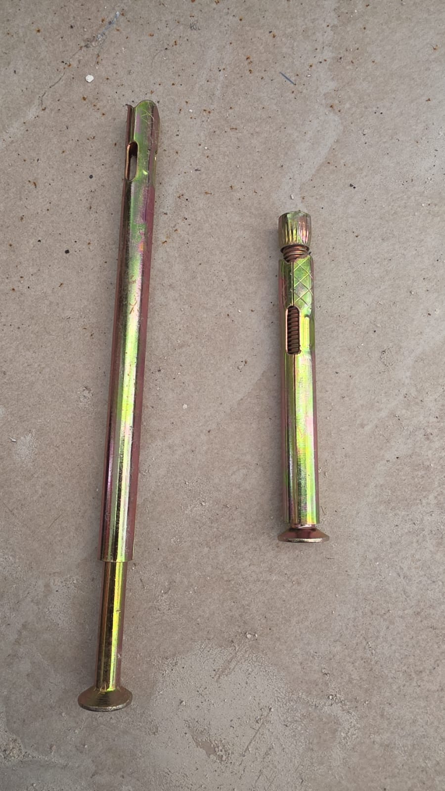 Two metal expansion anchors of different lengths on a concrete floor for home lift enclosure installation.