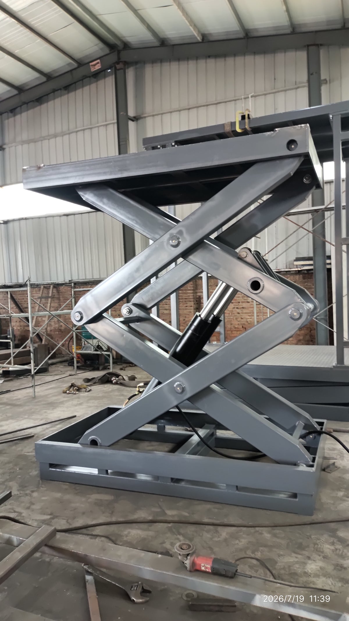 5-ton double scissor structure lift at mid-rise — angled view showing hydraulic ram, scissor pivot joints and base frame construction